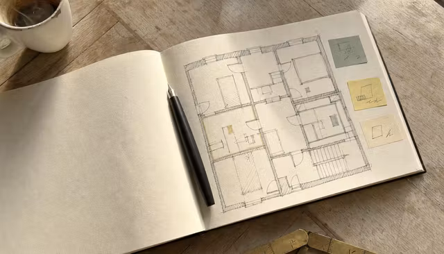Carnet d'architecte ouvert avec plan dessiné à l'encre noire et annotations colorées, ambiance d'atelier parisien