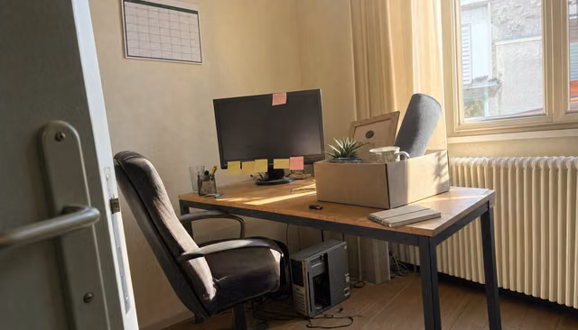 Bureau vacant d'un développeur dans une PME : carton de départ, écran éteint couvert de post-its, chaise vide