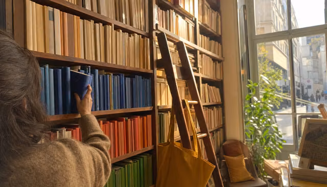 Main choisissant un livre bleu roi parmi des rangées de tranches colorées dans une librairie ensoleillée